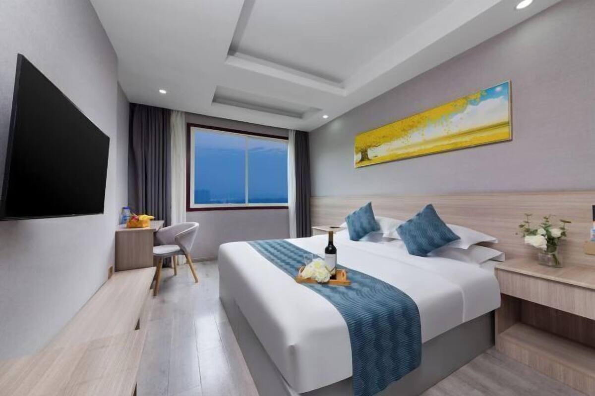 Quarto de hotel moderno com uma cama grande, televisão de tela plana, escrivaninha e janela com vista para a cidade.