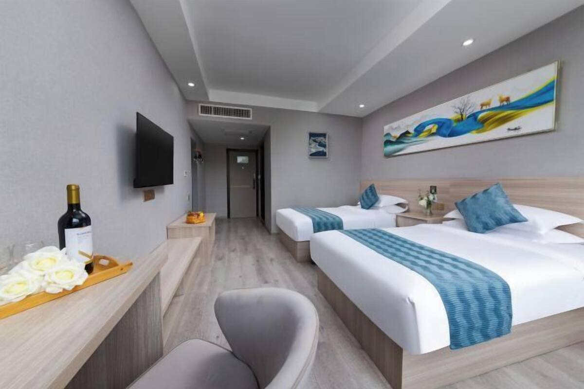 Quarto de hotel com duas camas, televisão, um quadro e uma garrafa de vinho no criado-mudo.
