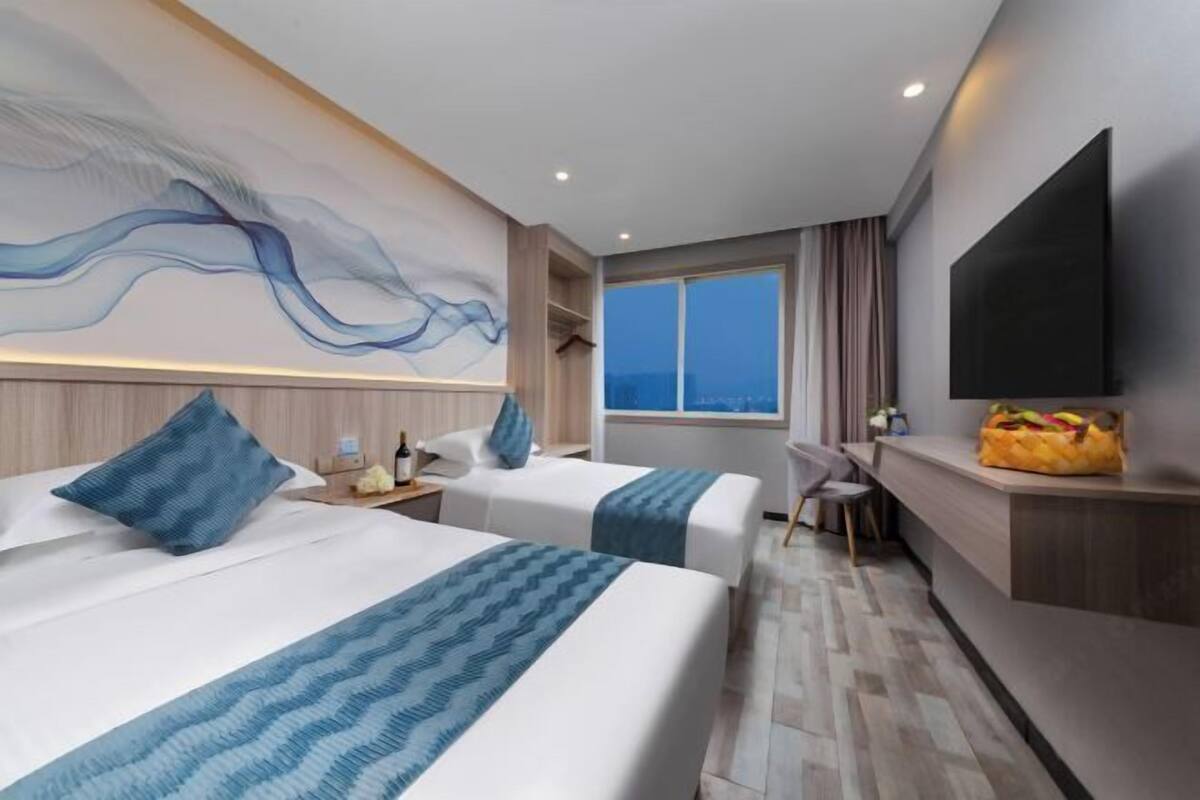 Quarto de hotel com duas camas, uma mesa, uma televisão e uma janela grande.