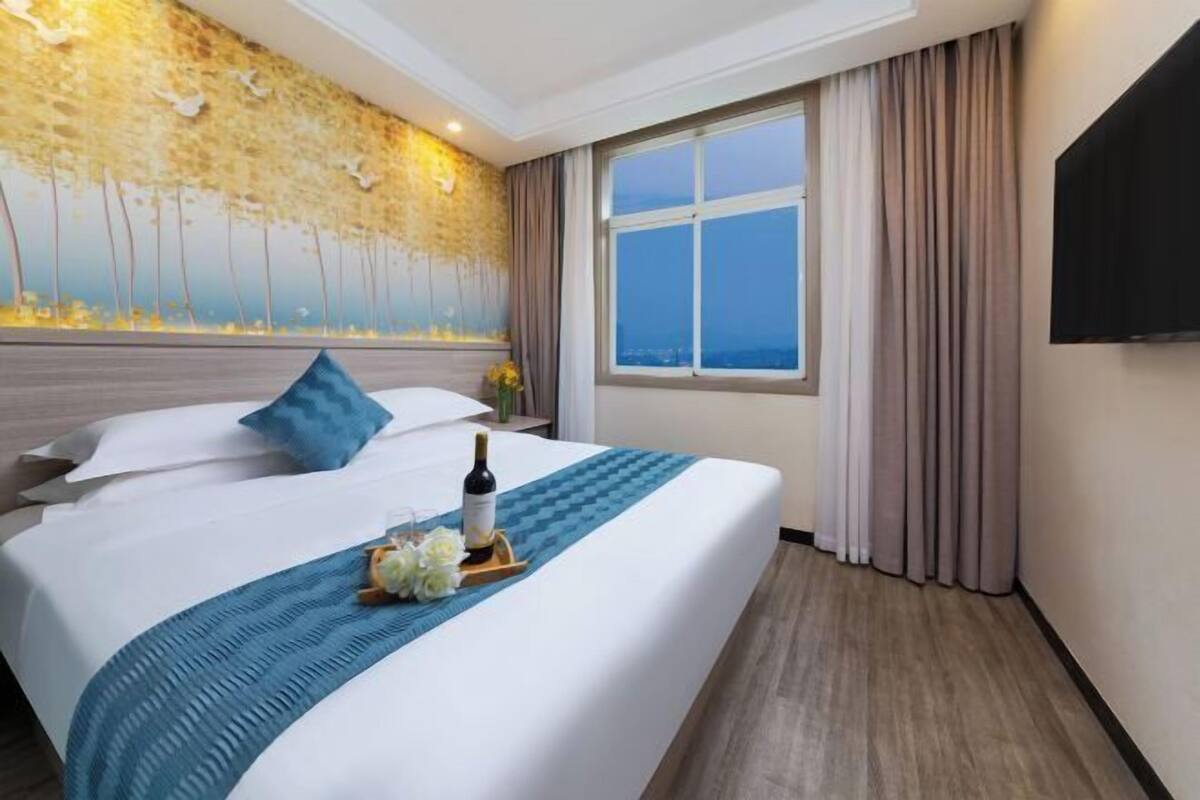 Quarto de hotel com uma cama grande, vista da cidade pela janela e uma TV de tela plana na parede.