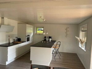 Una cocina moderna con armarios blancos, una isla central, un ventanal con vistas y una lámpara colgante.
