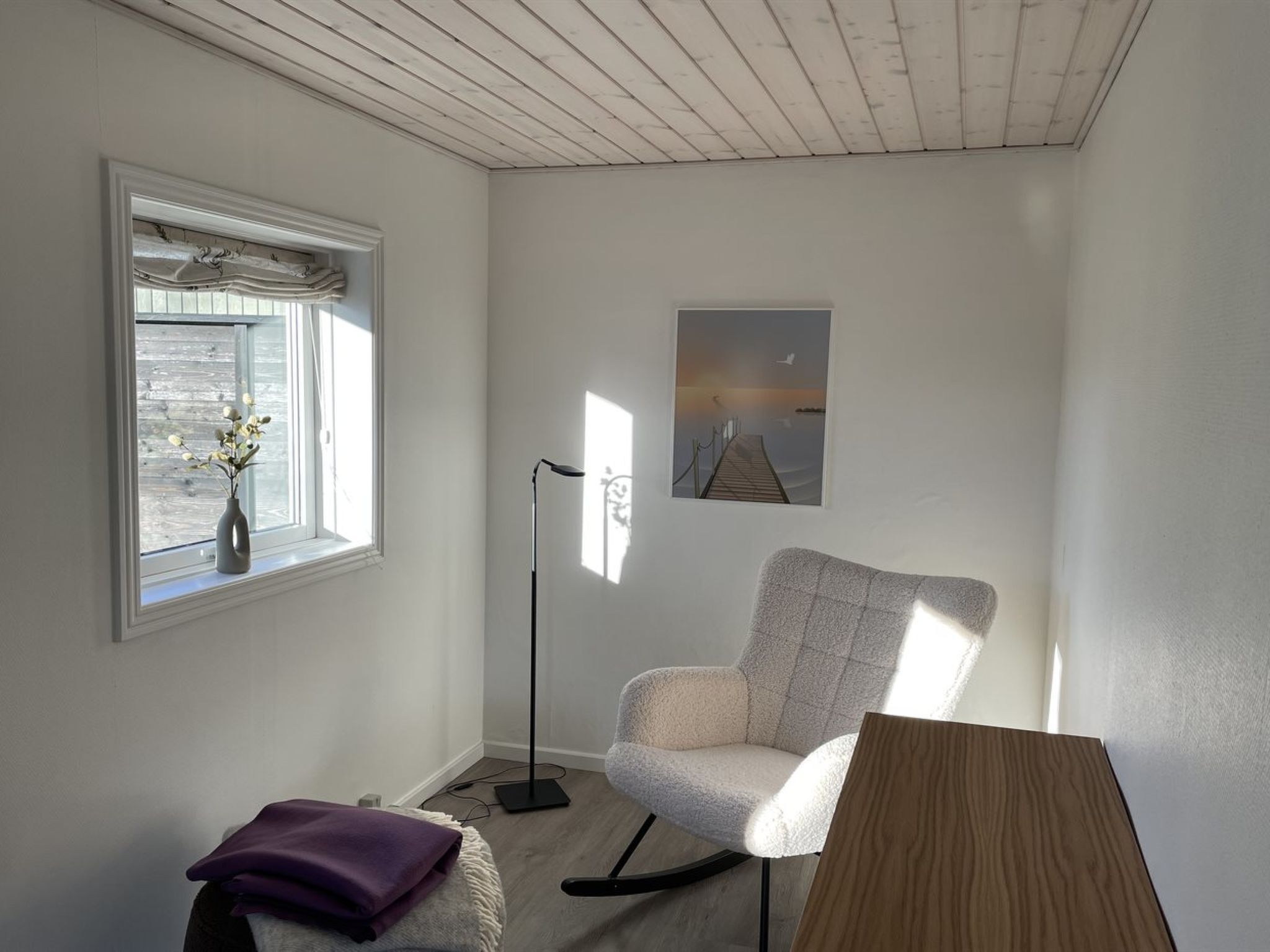 Una habitación de esquina con ventana, una silla, una lámpara de pie y un cuadro en la pared.