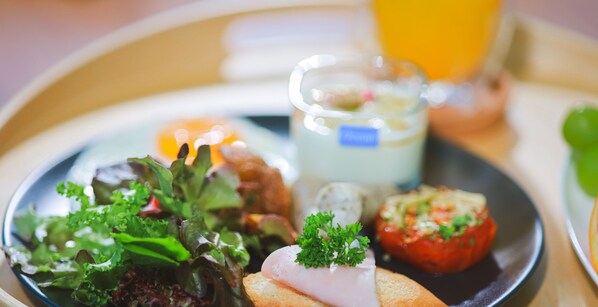 Une assiette contenant divers aliments, notamment une salade, un morceau de viande, un plat à base de tomates et un verre de jus.