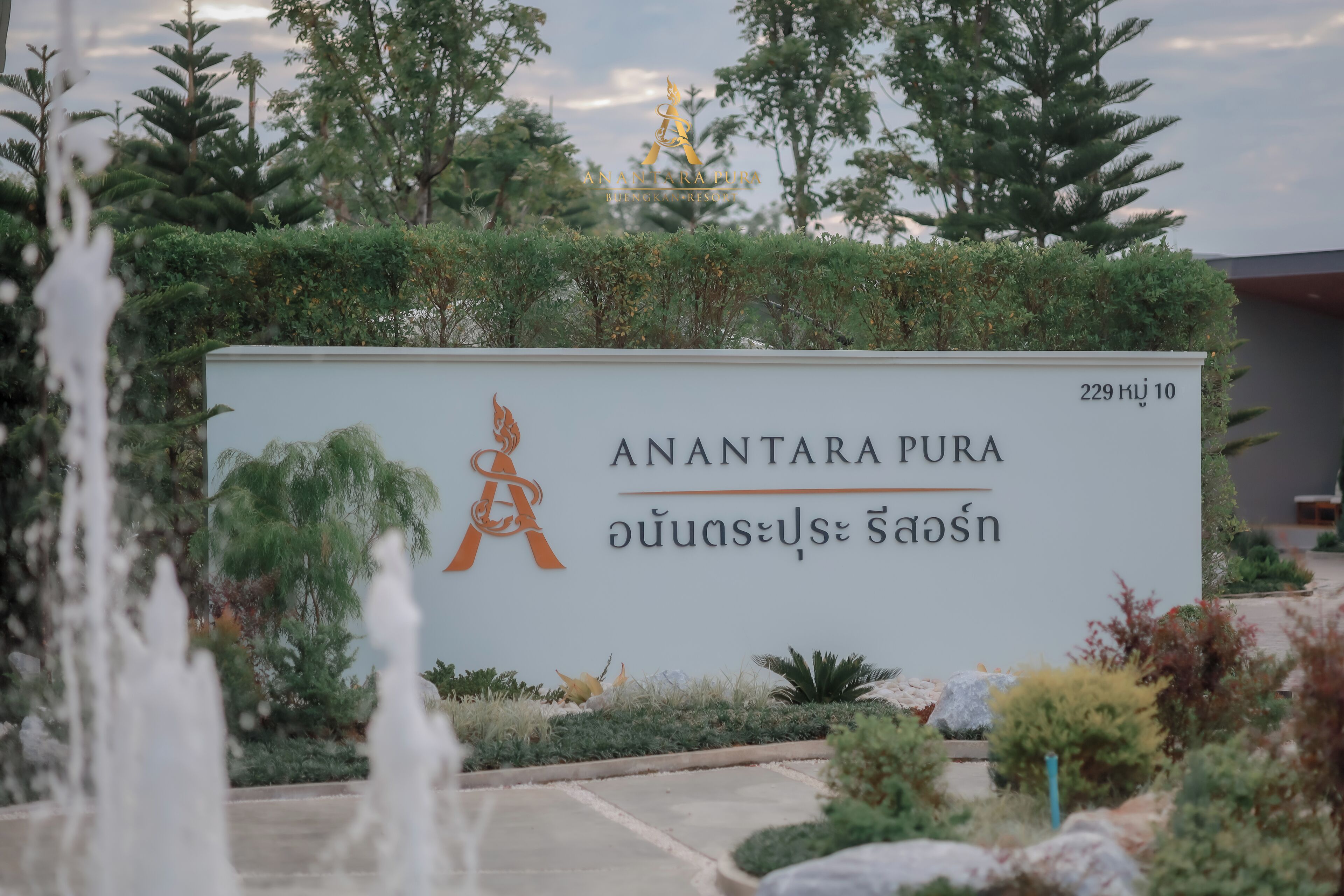 Indicador d'Anantara Pura amb text tailandès, envoltat de verdura i una font.