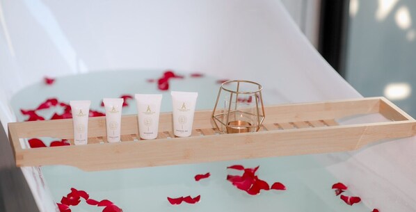 A wooden tray with five toiletry bottles and a candle on a bathtub with rose petals. - Anant Pura Resort (Bung Khong Long)