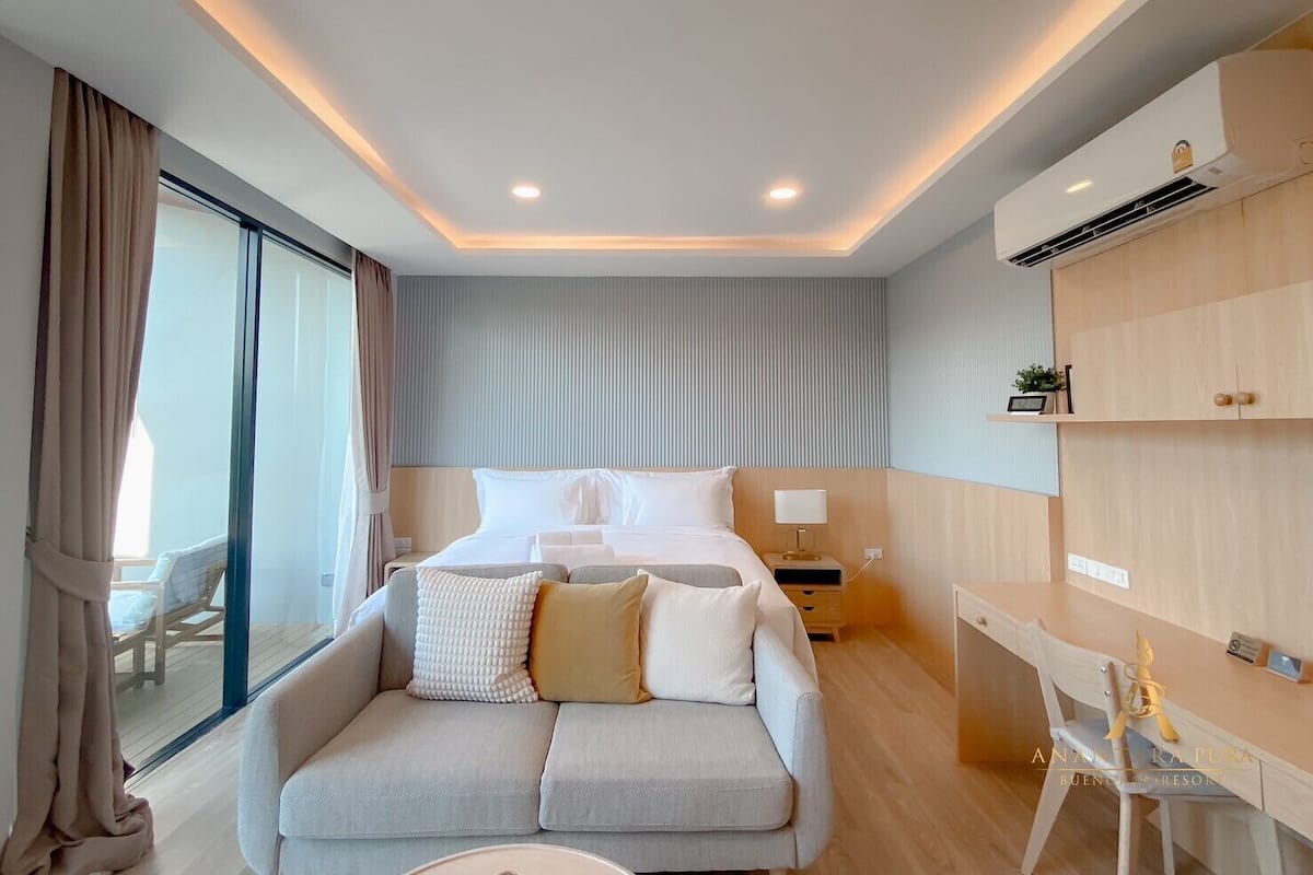 A modern hotel room with a large bed, a sofa, a desk, and a large window.