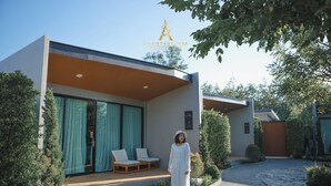 A modern building with a covered outdoor seating area, a stone pathway, and a well-maintained garden.