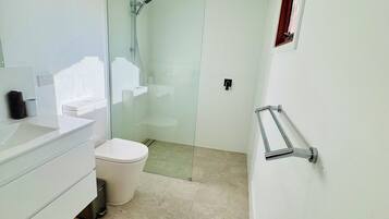 A modern bathroom with a glass shower enclosure, a toilet, a sink with a towel holder, and a small window.