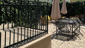 An outdoor patio area with a metal fence, outdoor furniture, and umbrellas.