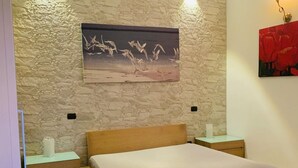 A bedroom with a bed, two bedside tables, a wall-mounted painting, and a wall-mounted light fixture.