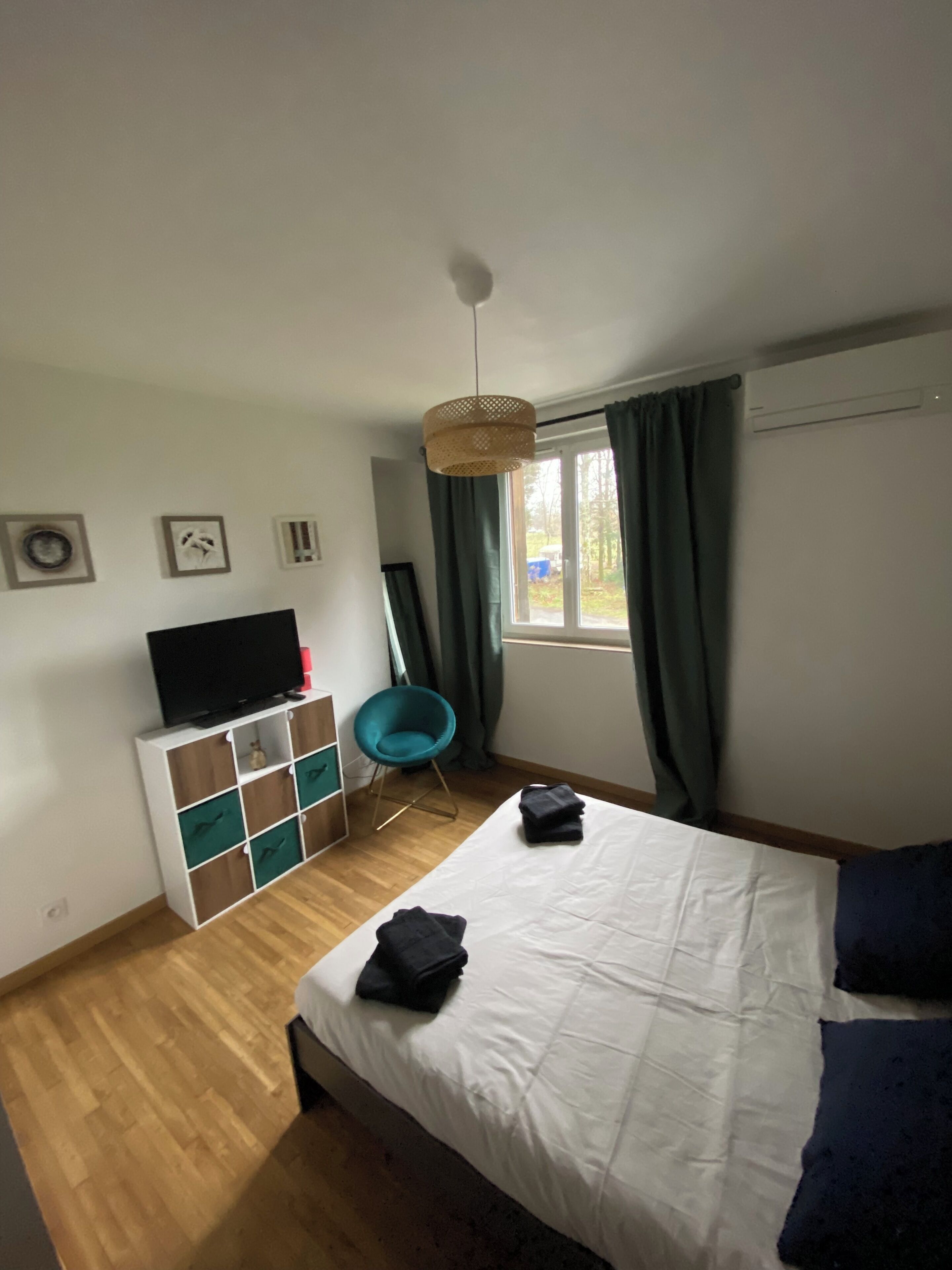Una camera da letto con un letto, una TV su un mobile bianco, una sedia e una finestra con tende.