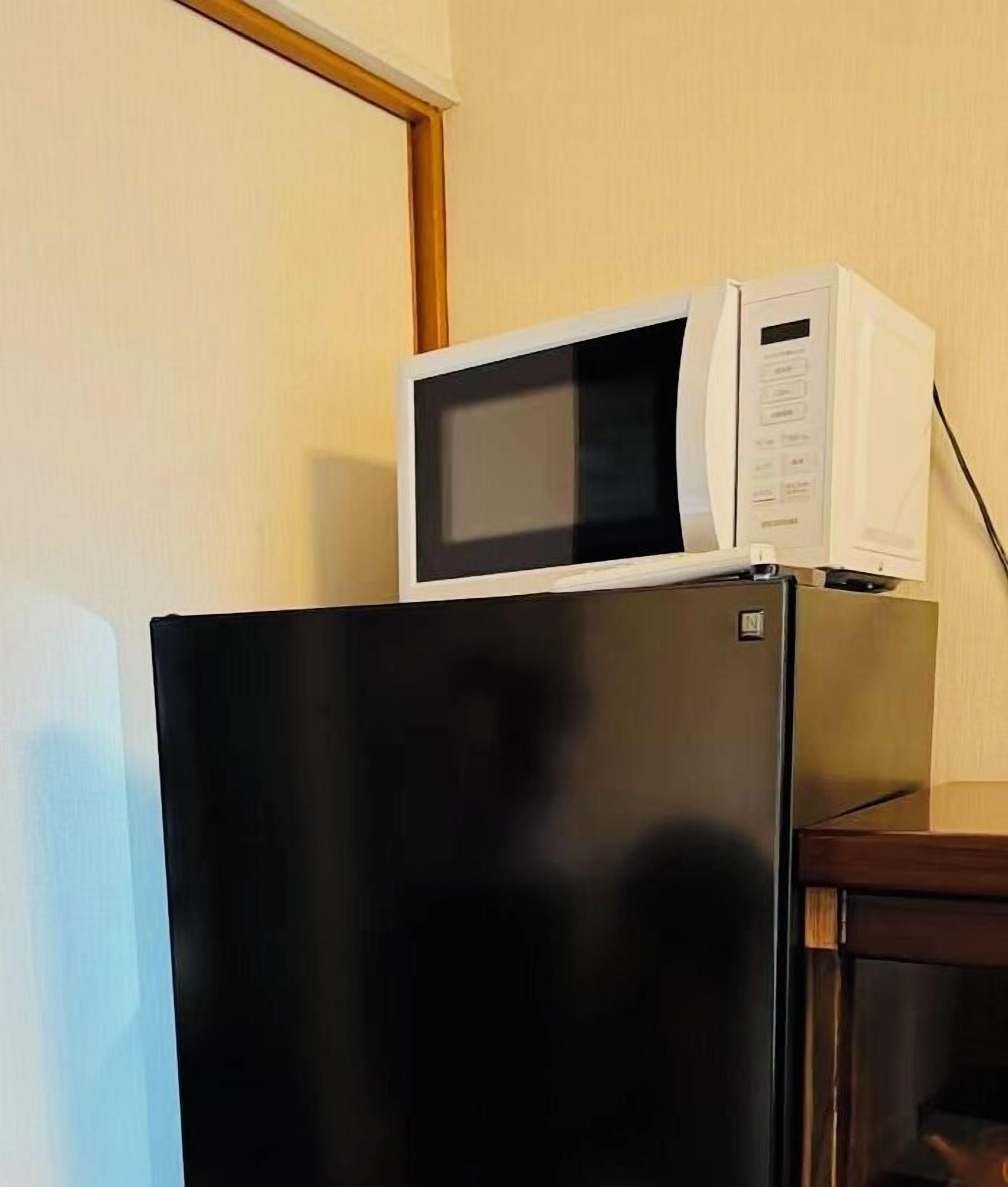 Un réfrigérateur noir avec un four à micro-ondes posé sur le dessus, une table en bois et un mur de couleur beige.