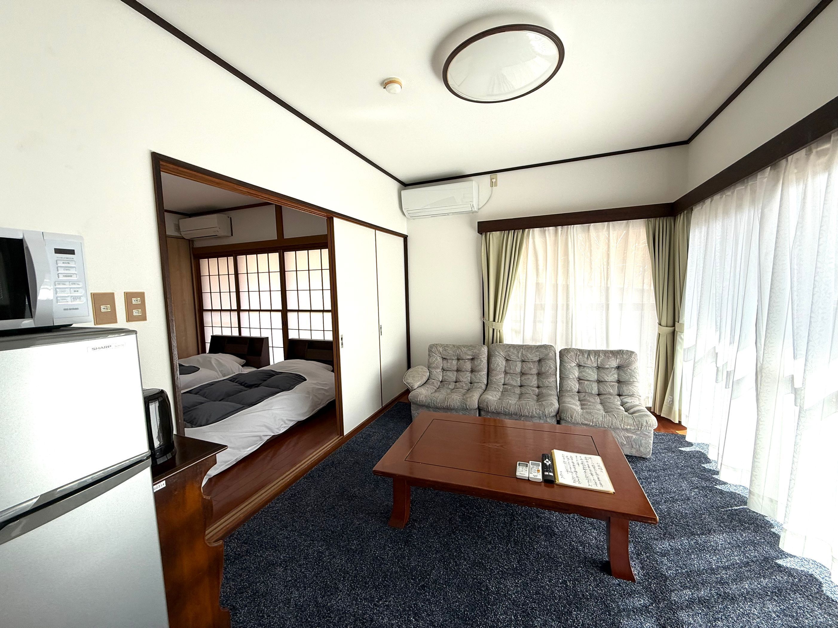 A hotel room with a bed, a sofa, a coffee table, a microwave, and an air conditioning unit.