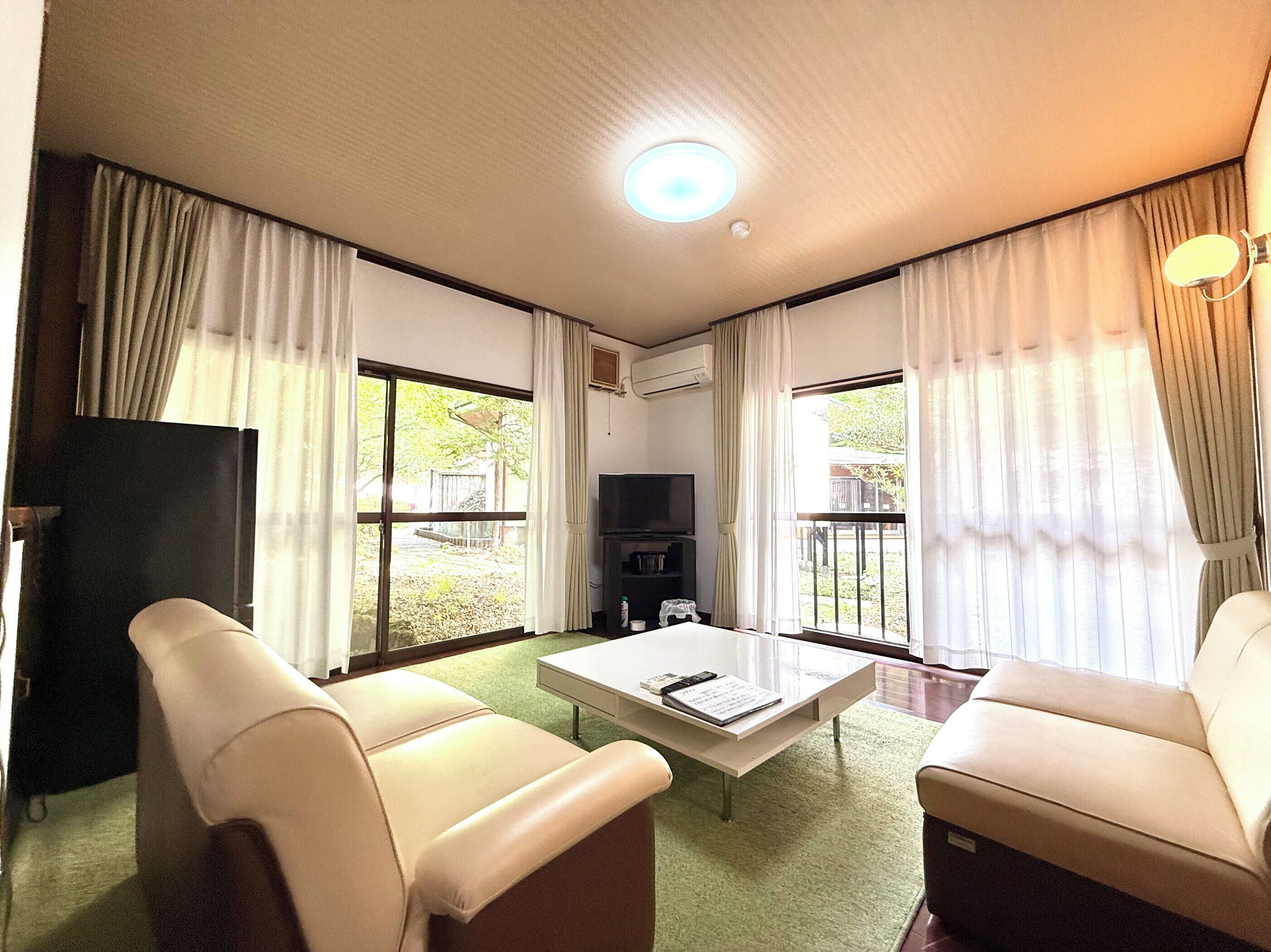 A room with two beige sofas, a coffee table, a TV, and large windows with curtains.