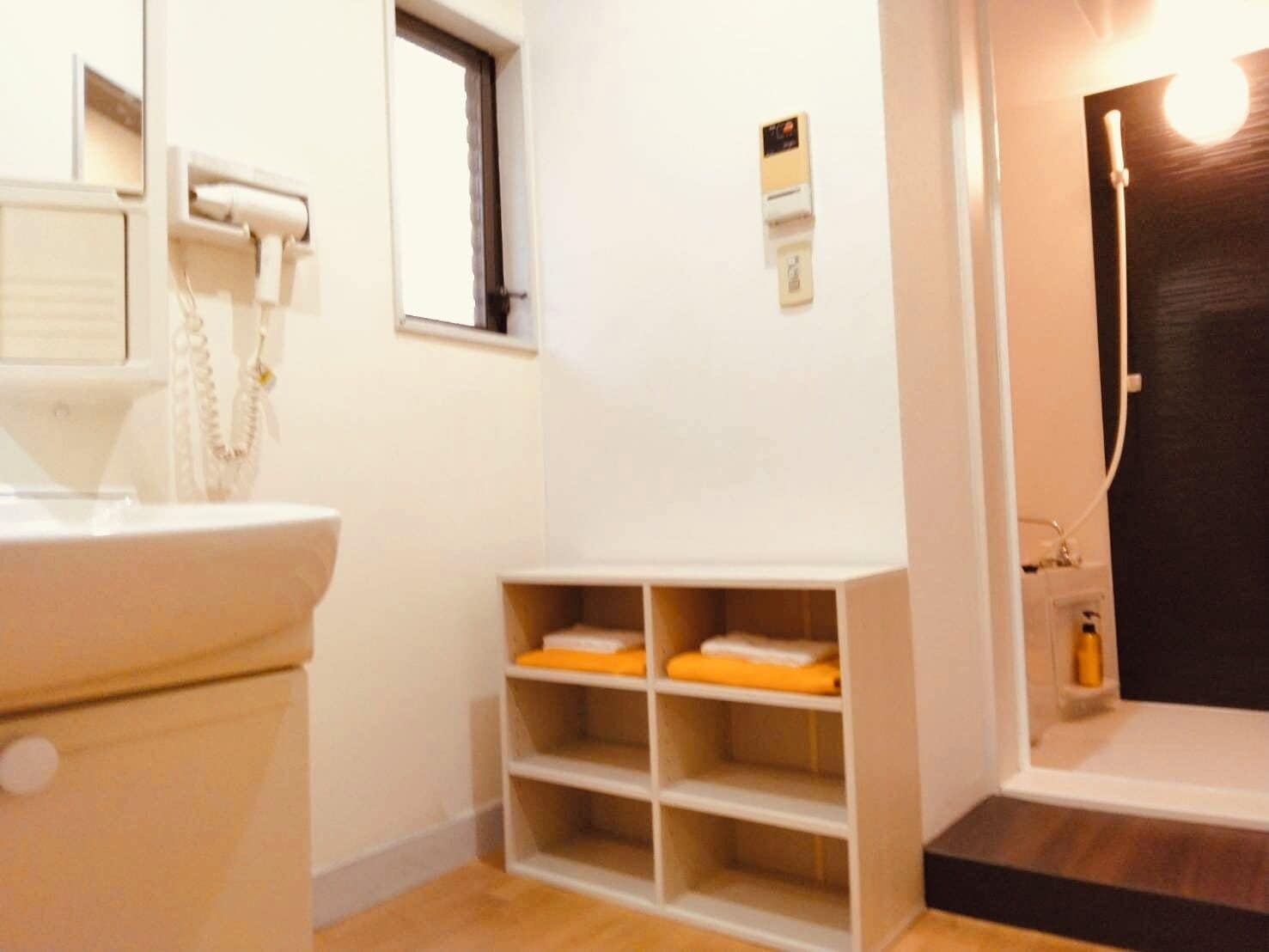 A bathroom with a white sink, a mirror, a window, and a shelf with folded towels.