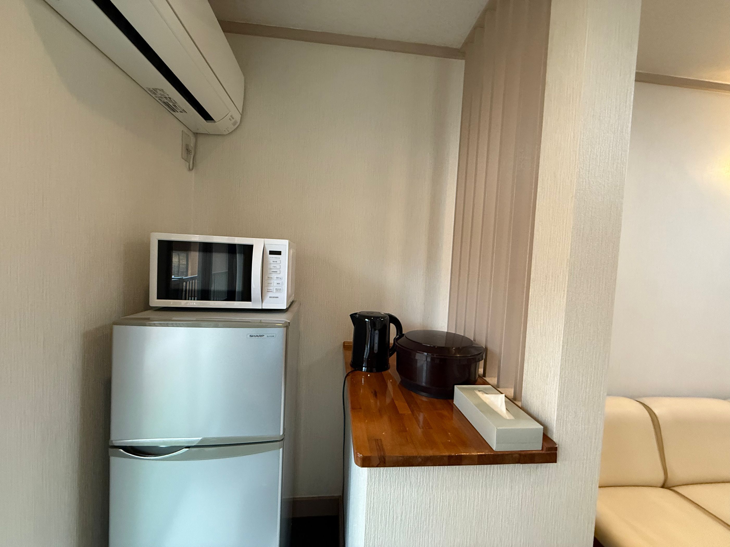 A compact kitchenette with a microwave, a small refrigerator, a coffee maker, and a tissue box on a wooden shelf.