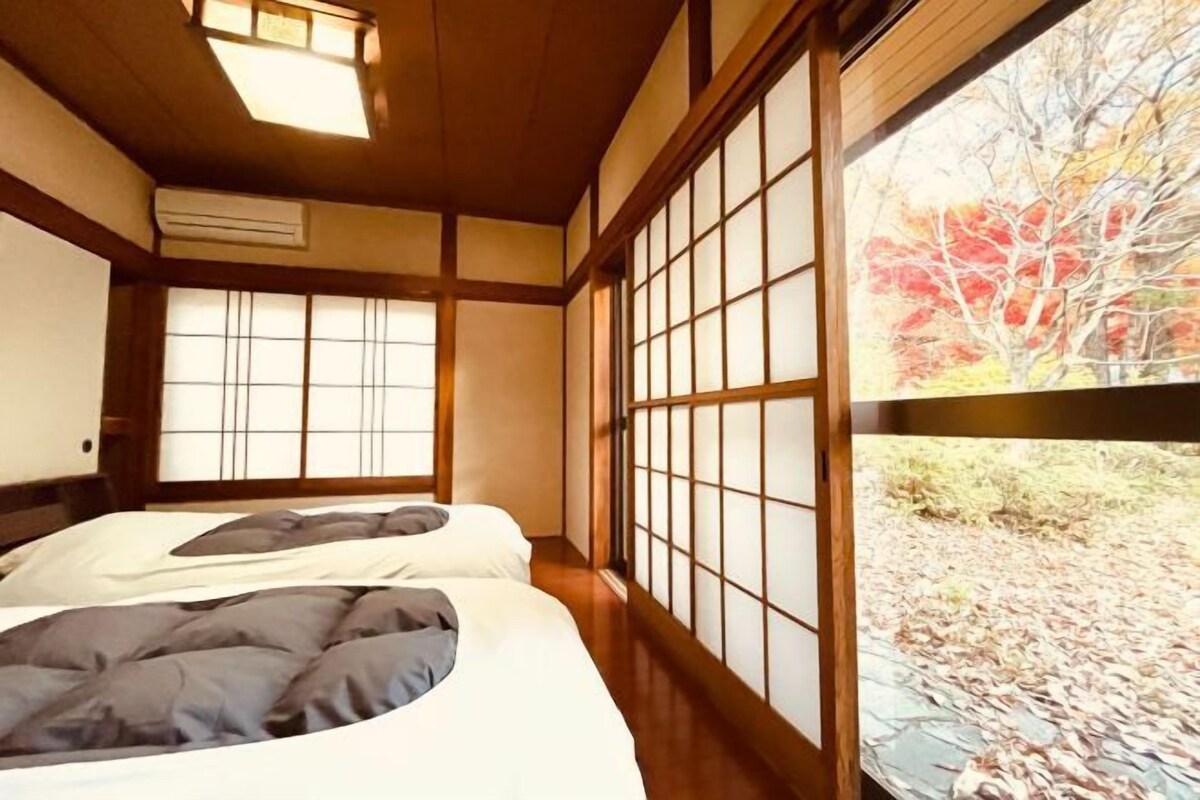 Een traditionele Japanse kamer met tatami vloeren, schuifdeuren en een groot raam met uitzicht op herfstkleuren.