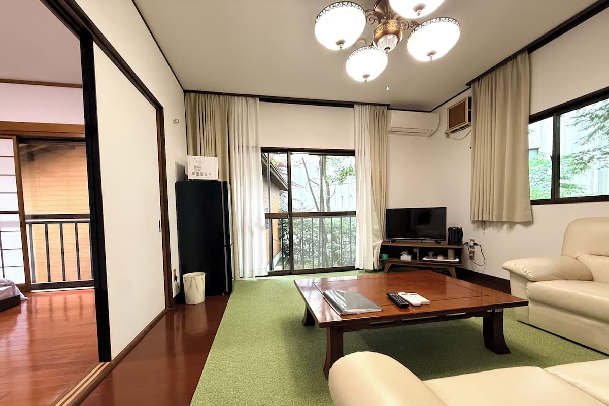 Una sala de estar con sofá, mesa de centro, televisor y un amplio ventanal con cortinas.