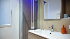 Un baño moderno con un lavamanos blanco, un espejo y una zona de ducha.