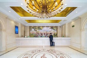 A hotel lobby with a reception desk, a large chandelier, and a mural on the wall. - Vianna Hotel (Kunming)