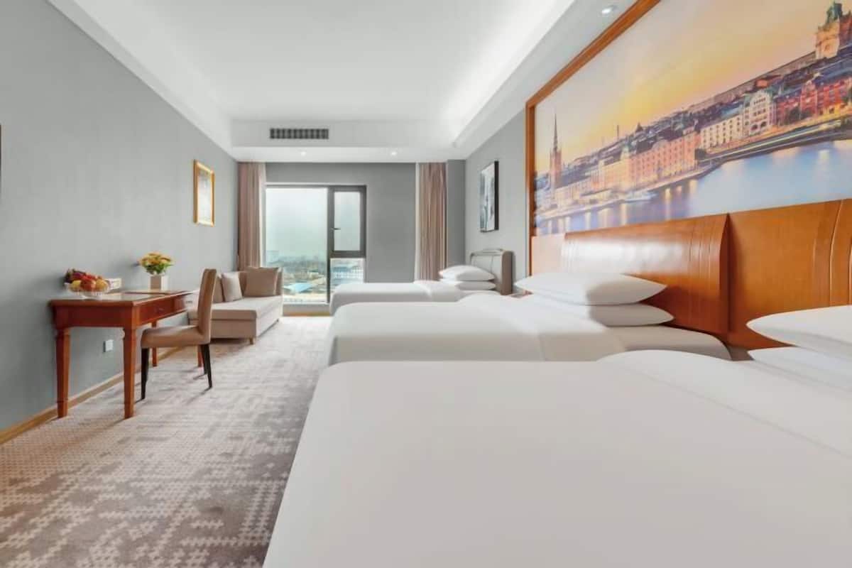 Hotellihuone, jossa on suuri sänky, työpöytä, tuoli ja näkymä kaupunkimaisemaan.