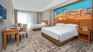 Ein Hotelzimmer mit zwei Betten, einem Schreibtisch, einem Stuhl und einem großen Gemälde an der Wand.