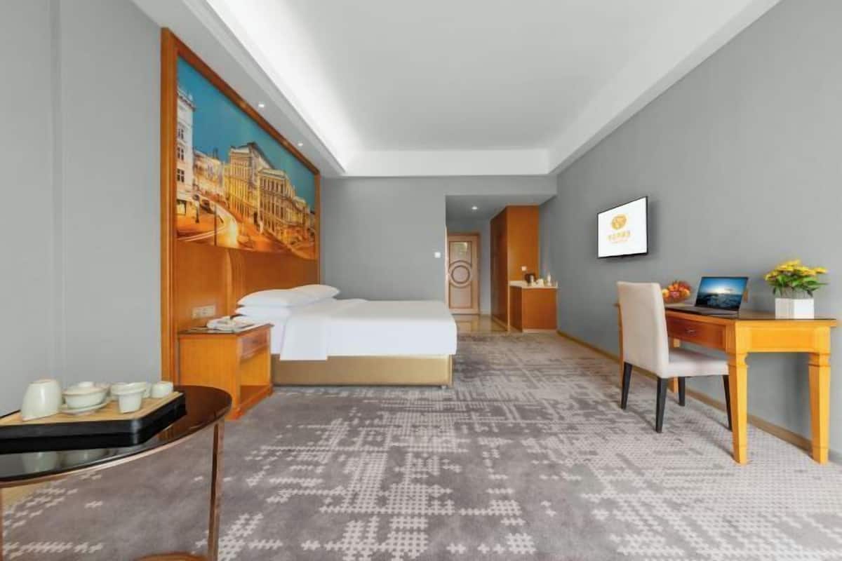 Hotellihuone, jossa on sänky, työpöytä, tuoli ja taulu seinällä.