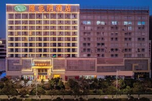 A multi-story hotel with a prominent sign, a ground-level entrance, and a parking area in front. - Vianna Hotel (Kunming)