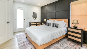 Ein Schlafzimmer mit Bett, Nachttisch, Deckenventilator, Tür und Fenster mit Jalousien.