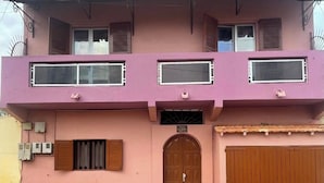 Un bâtiment à deux étages avec une façade rose, une porte centrale en arc de cercle et un portail marron.