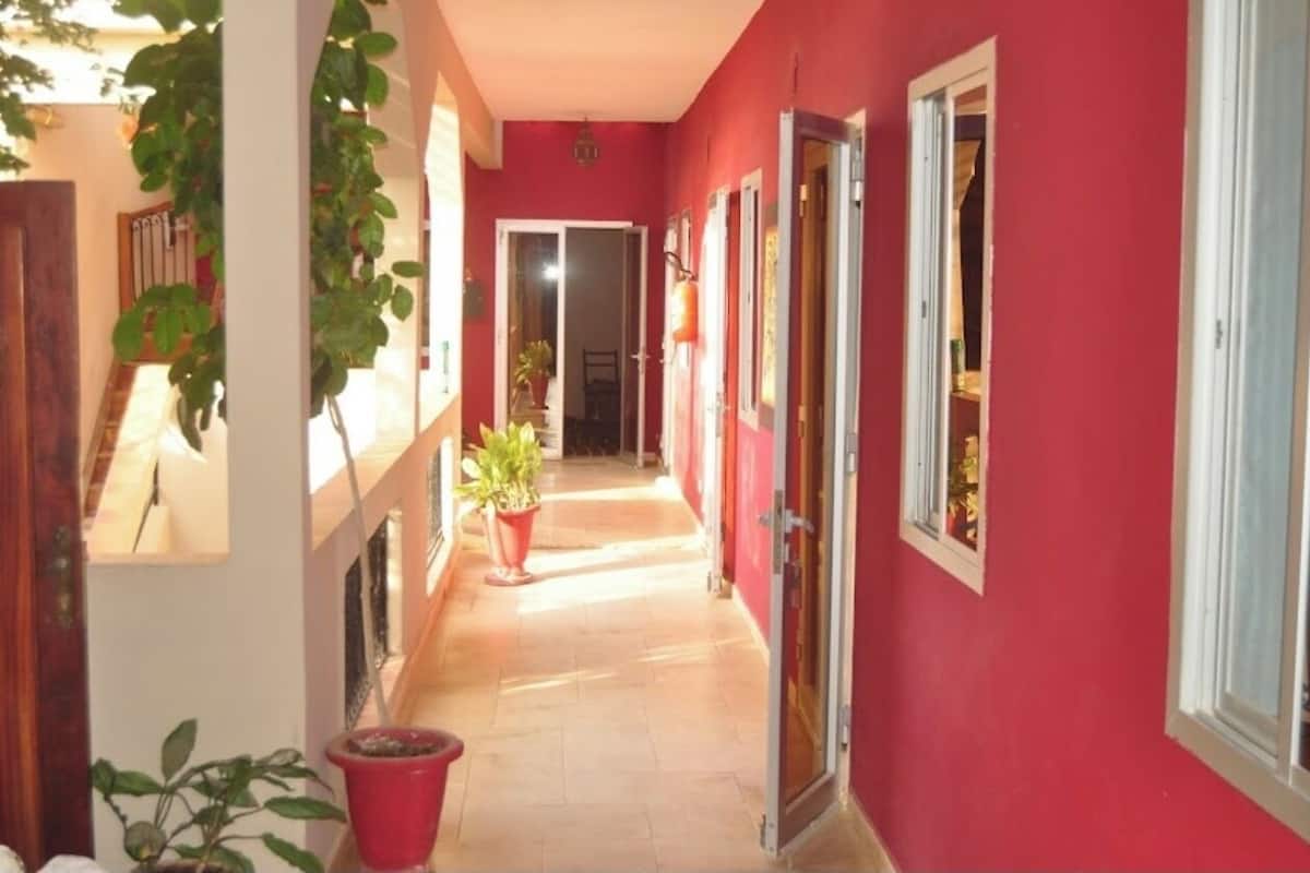 A narrow hallway with red walls and a tiled floor, leading to a door at the end.