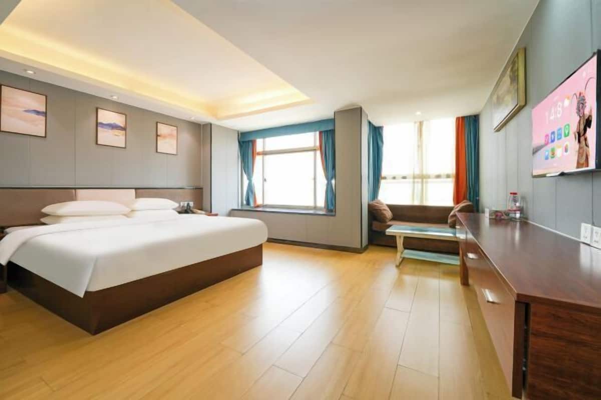 Habitación de hotel con una cama grande, un escritorio, un ventanal con cortinas y obras de arte en las paredes.