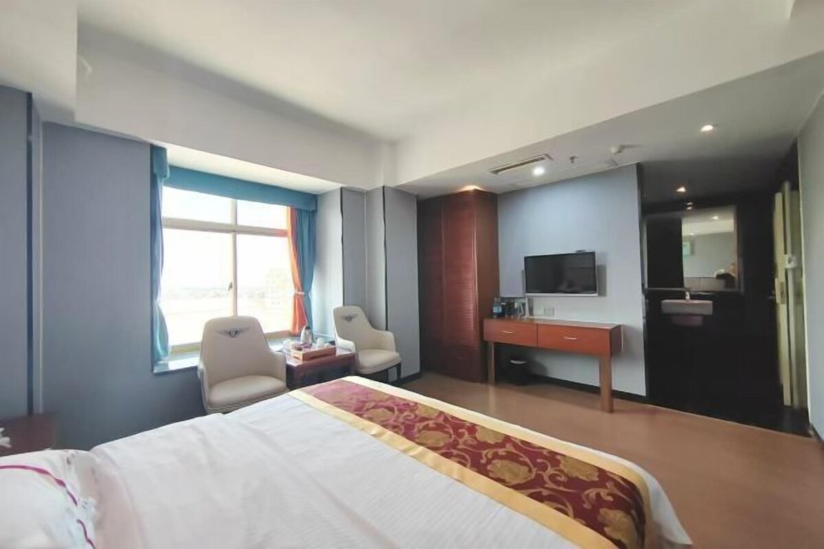 A hotel room with a bed, two chairs, a desk, a television, and a bathroom.