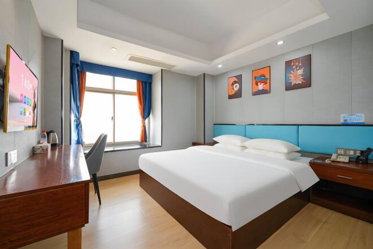 Una habitación de hotel con cama, escritorio, silla, ventana con cortinas y decoración en la pared.