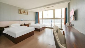 A hotel room with two beds, a desk, a chair, a TV, and a large window.