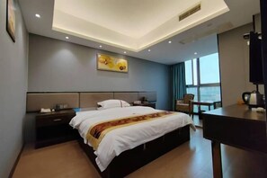 A hotel room with a bed, bedside table, desk, chair, and a painting on the wall.
