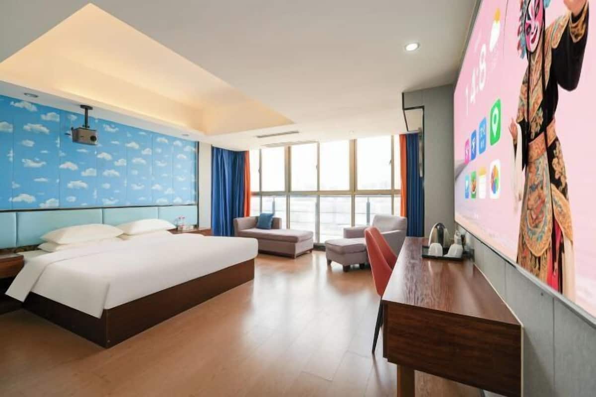 Una habitación de hotel con cama, escritorio, silla, sofá y un amplio ventanal.