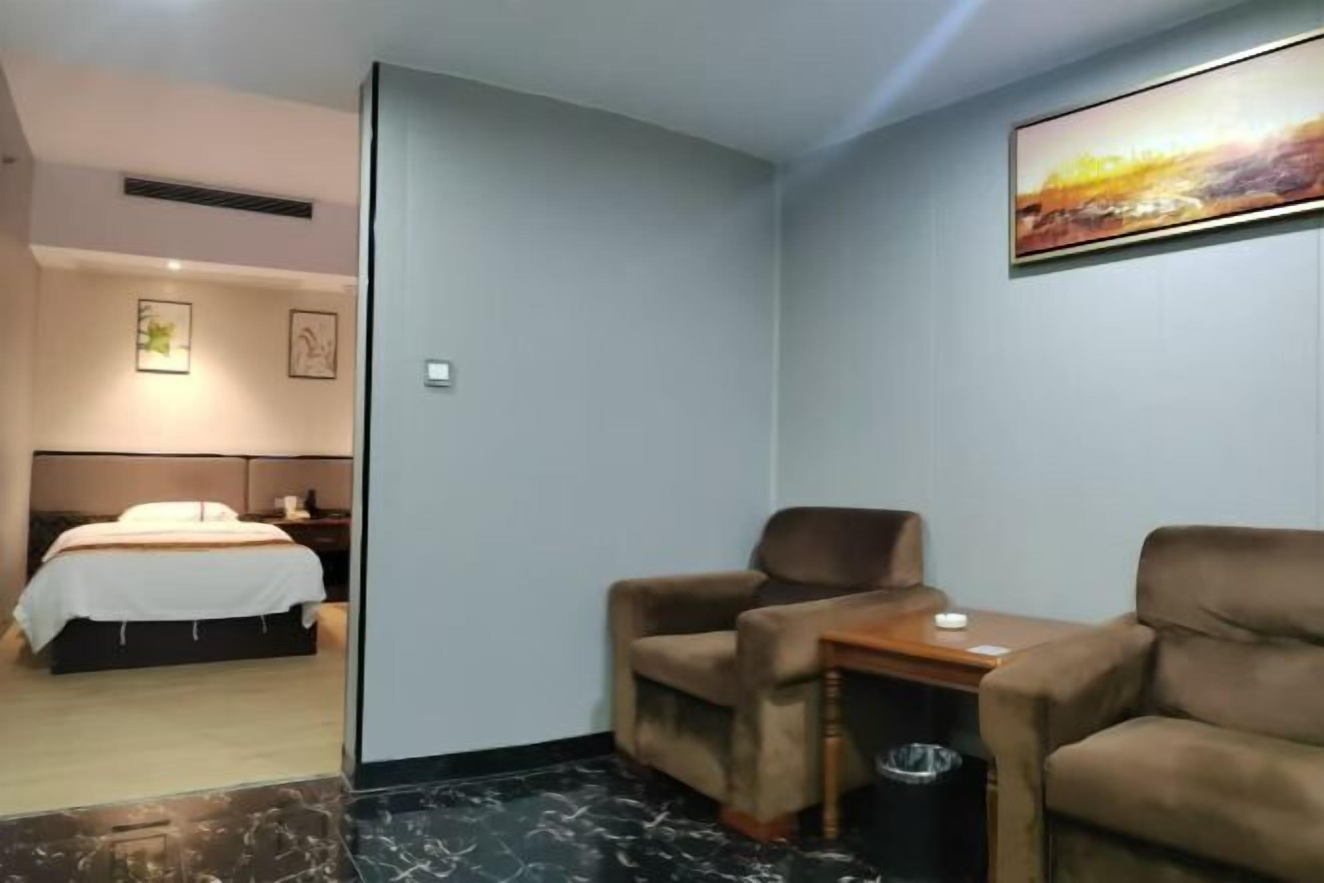 Una habitación de hotel con cama, escritorio, dos sillas, un cubo de basura y un cuadro en la pared.