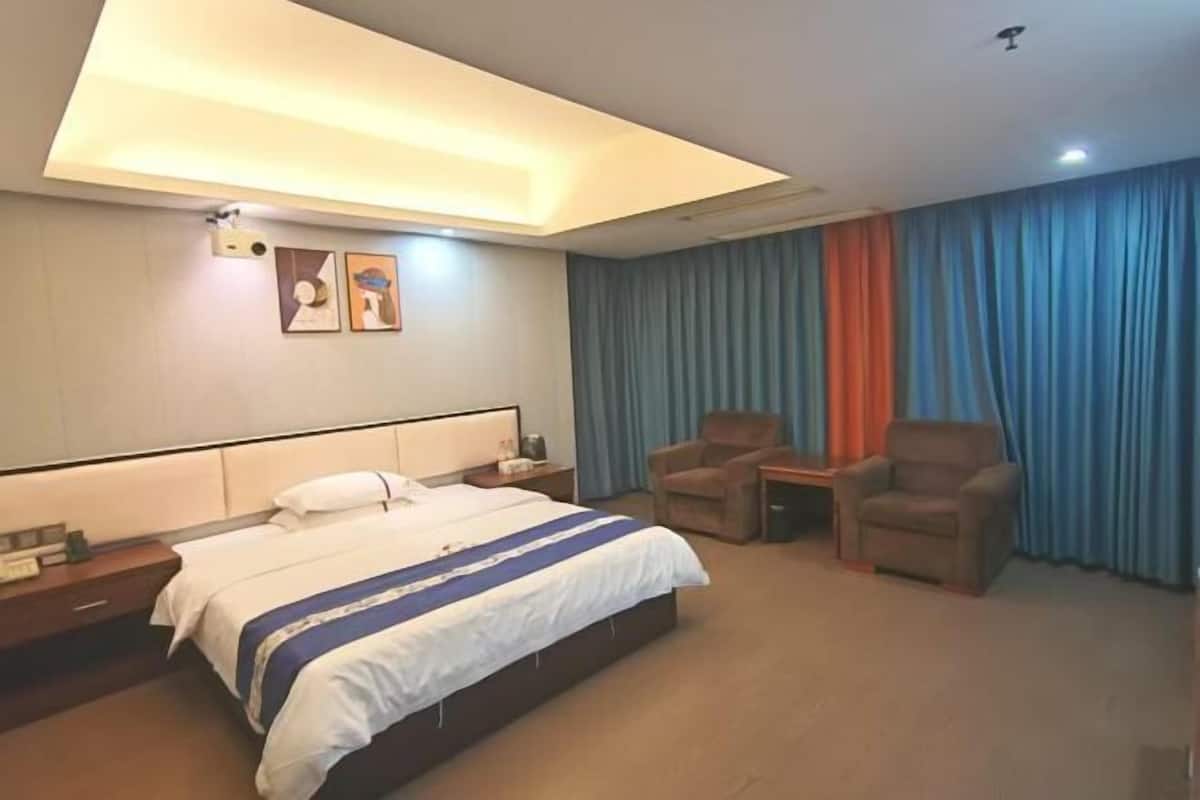 Una habitación de hotel con una cama, dos sillones, una mesita y una lámpara en el techo.