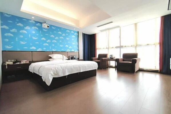 A hotel room with a large bed, a desk, two chairs, and a window with curtains.