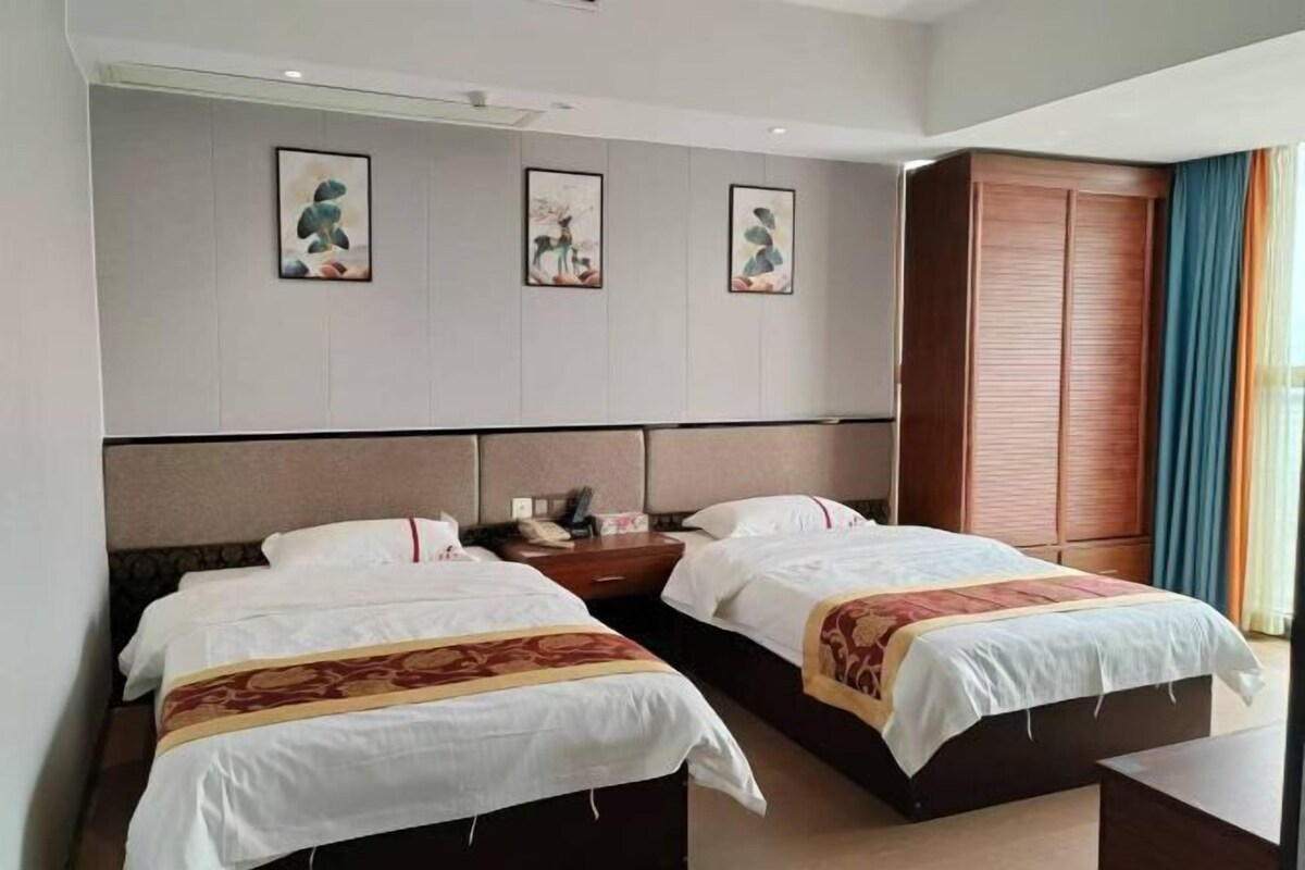 A hotel room with two beds, a wooden wardrobe, and three framed artworks on the wall.