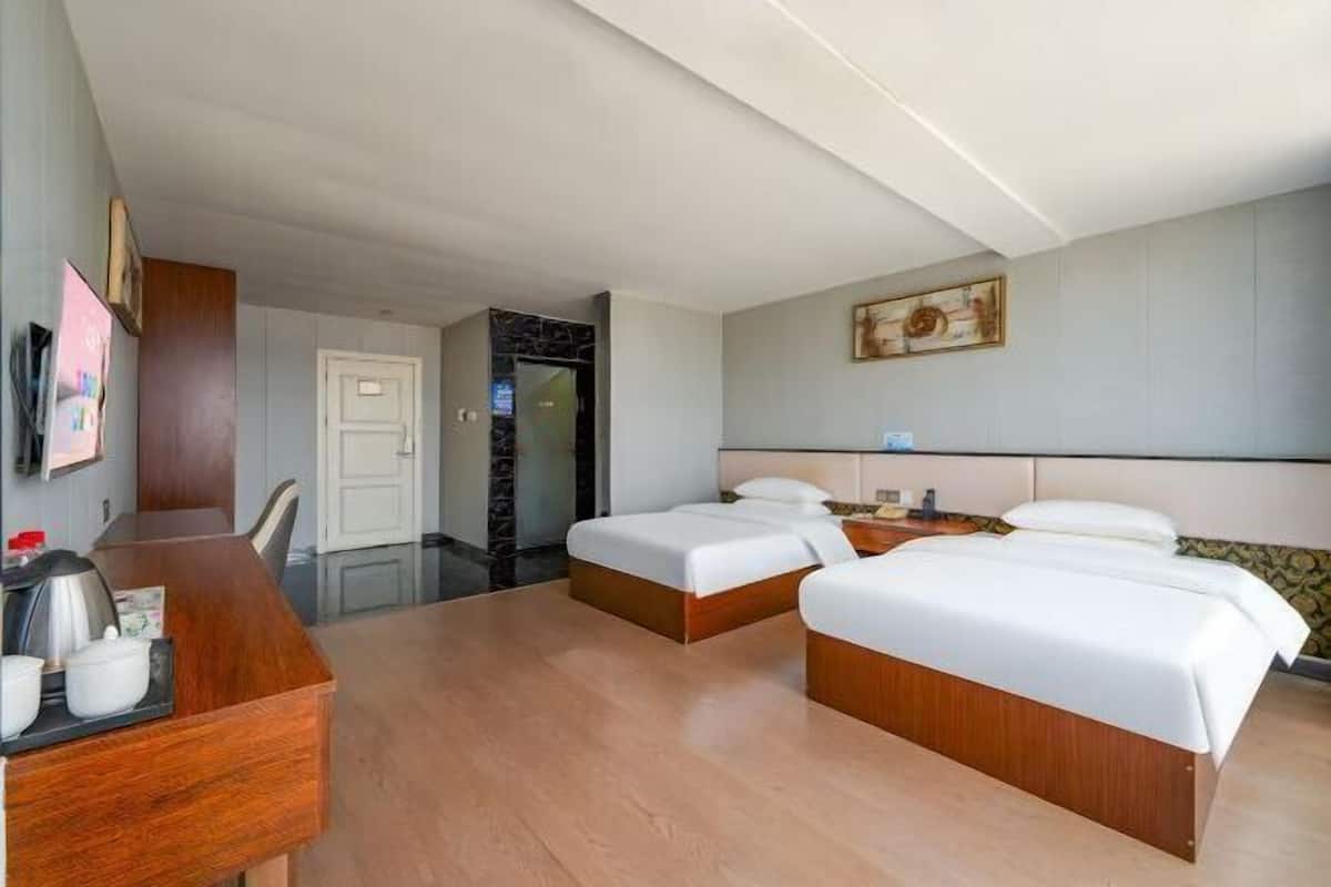 Habitación de hotel con dos camas, un escritorio, una silla, una cafetera y una puerta que da a un baño.