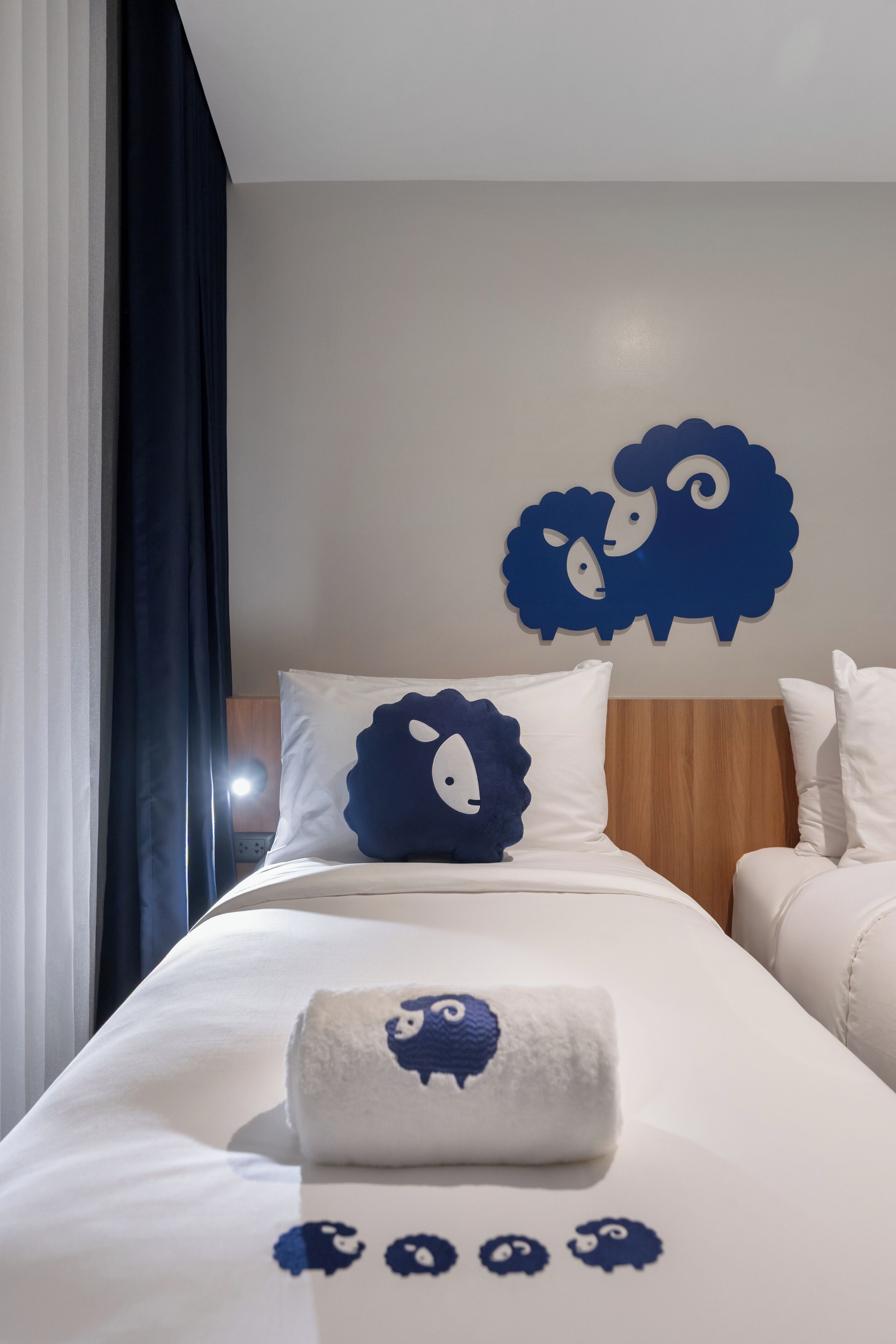 A hotel room with a bed featuring a blue sheep wall decoration, white bedding, and a neatly made bed with a blue and white pillow.