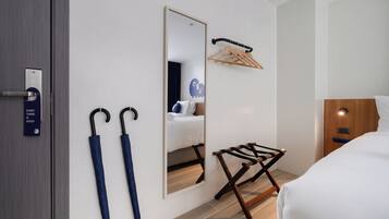 Quarto de hotel com porta de madeira, espelho, cama, cabideiro e dois guarda-chuvas.