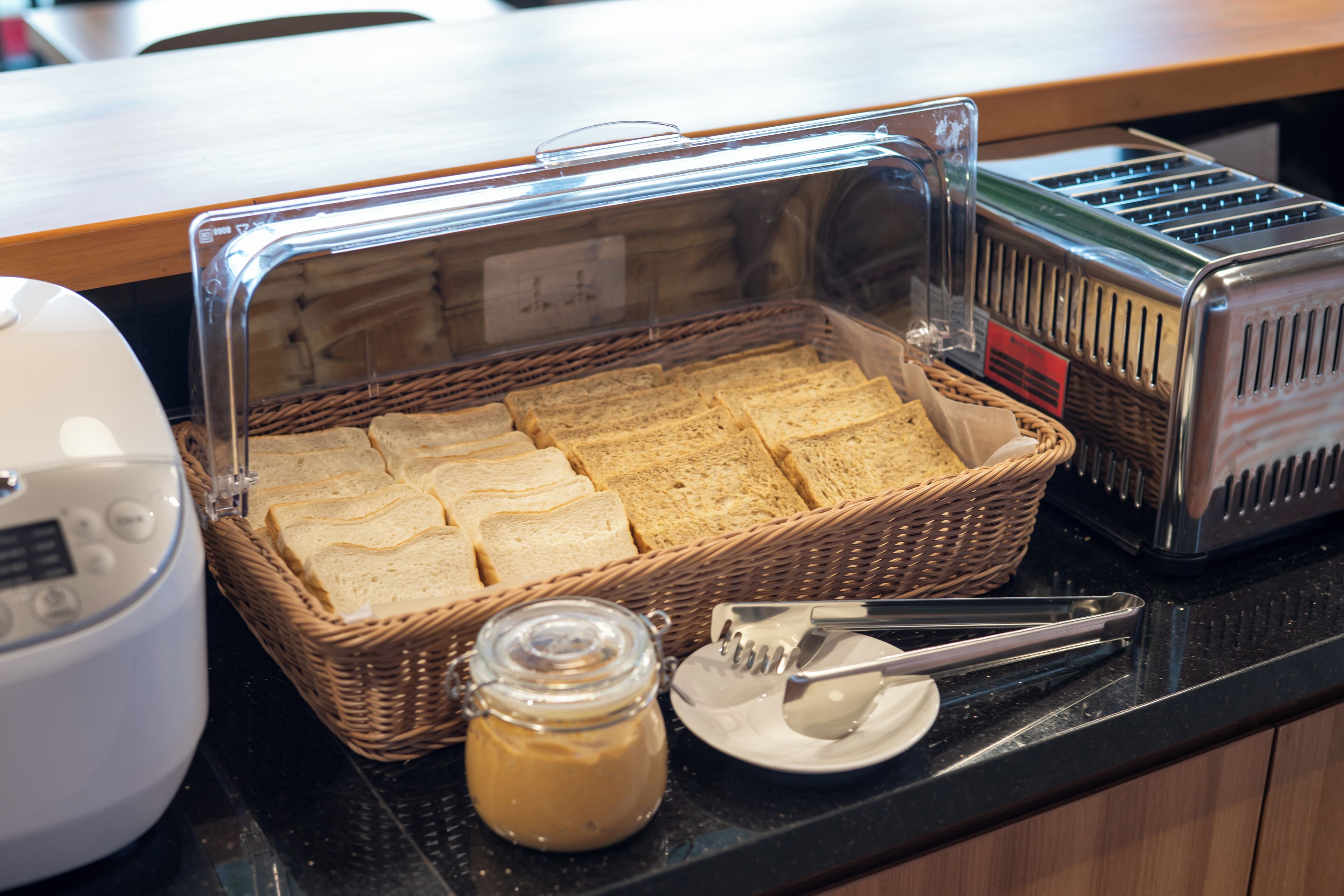 Un bufé de desayuno con pan rebanado, un tarro de mermelada y un tostador sobre una encimera.