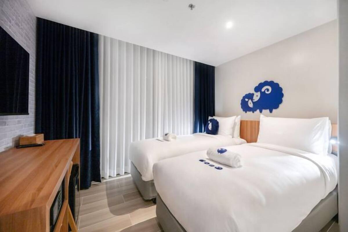 Une chambre d’hôtel avec deux lits, un bureau et une grande fenêtre avec des rideaux.