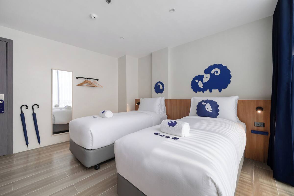 Une chambre d’hôtel avec deux lits, un miroir, un porte-manteau et une tête de lit en bois.