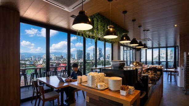 Un café moderne offrant une vue sur la ville, avec des meubles en bois et des lampes suspendues.