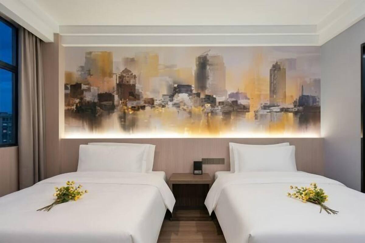 Habitación de hotel con dos camas, un cuadro de paisaje urbano en la pared y una mesita de noche entre ellas.