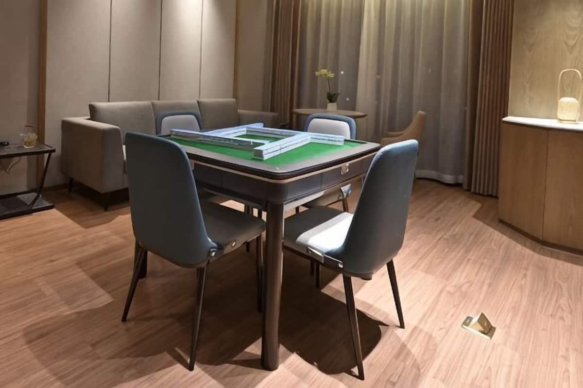 A room with a green felt table for playing card games, a sofa, and a small side table with a lamp.